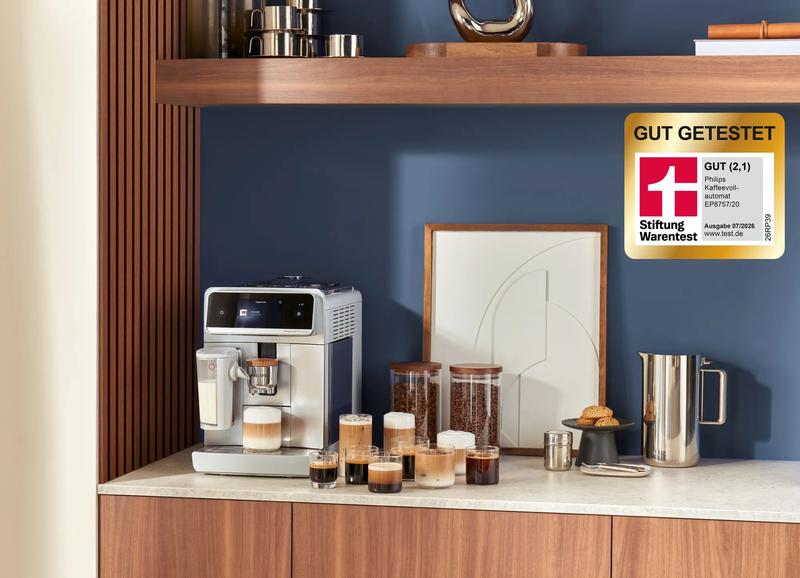 Ein Philips Kaffeevollautomat auf einer Küchenarbeitsplatte mit mehreren Tassen Kaffeegetränken, Gläsern mit Bohnen und einem Krug daneben.