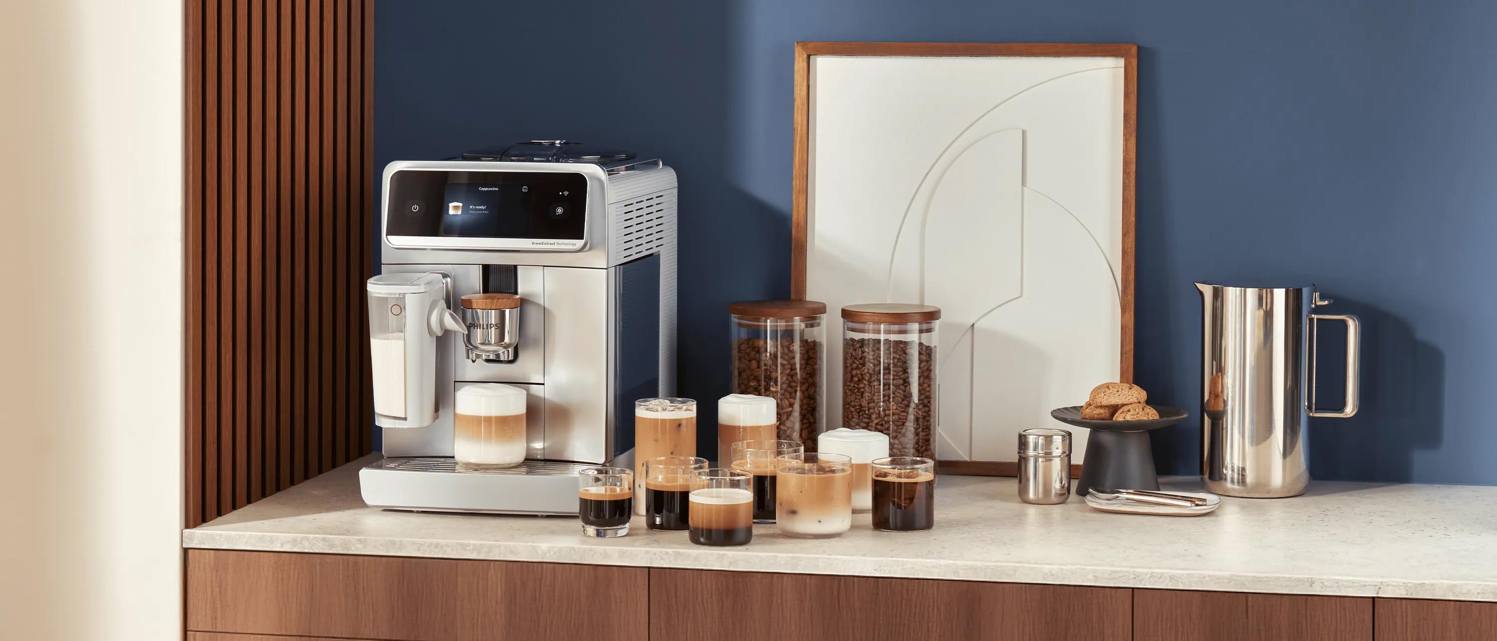 En automatisk espressomaskine fra Philips på et køkkenbord med flere kopper kaffe, krukker med bønner og en kande ved siden af.