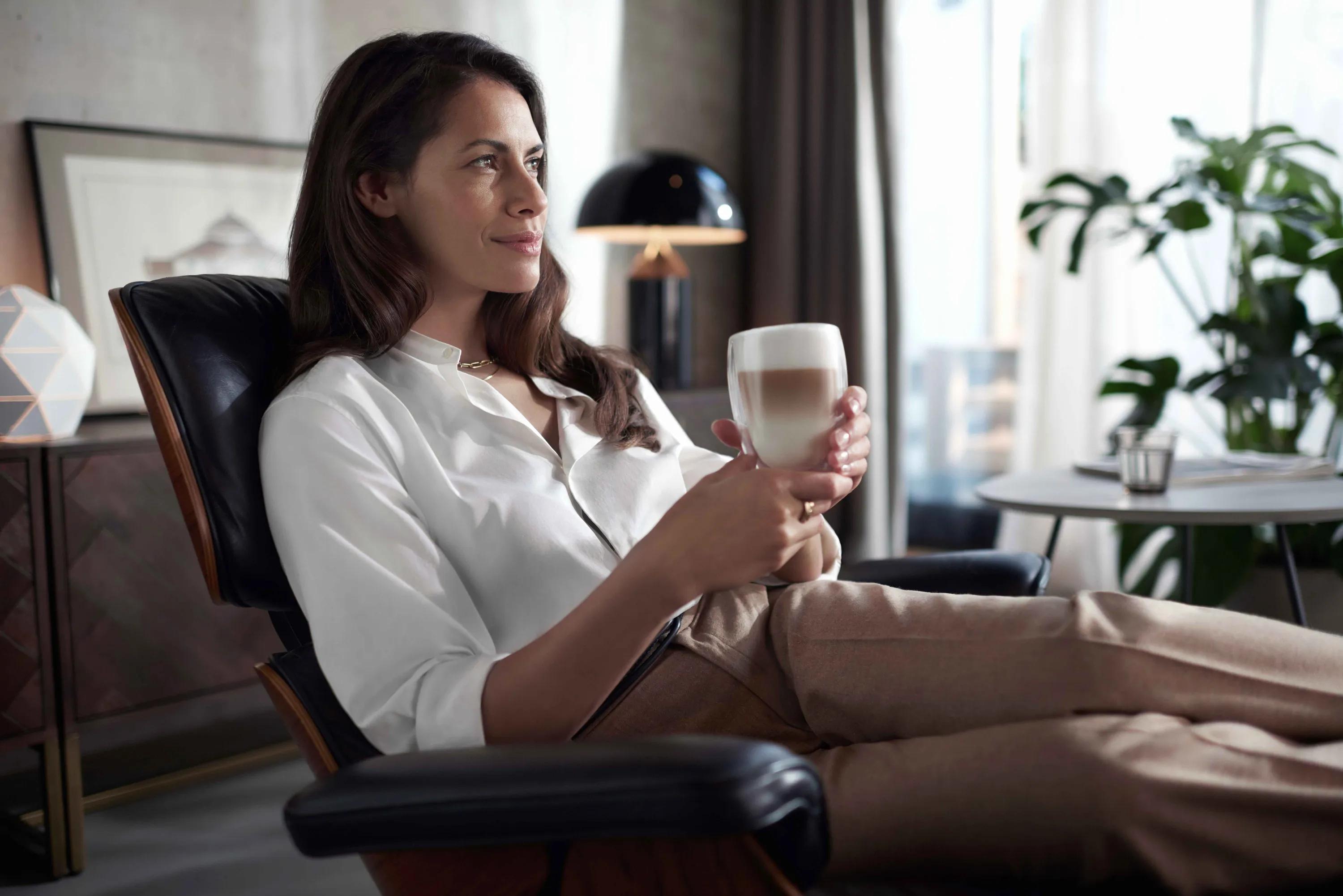 Frau entspannt sich, hält Schichtkaffee von Philips Saeco Xelsis. Vermittelt persönlichen Luxus und Premium-Kaffeeerlebnis.