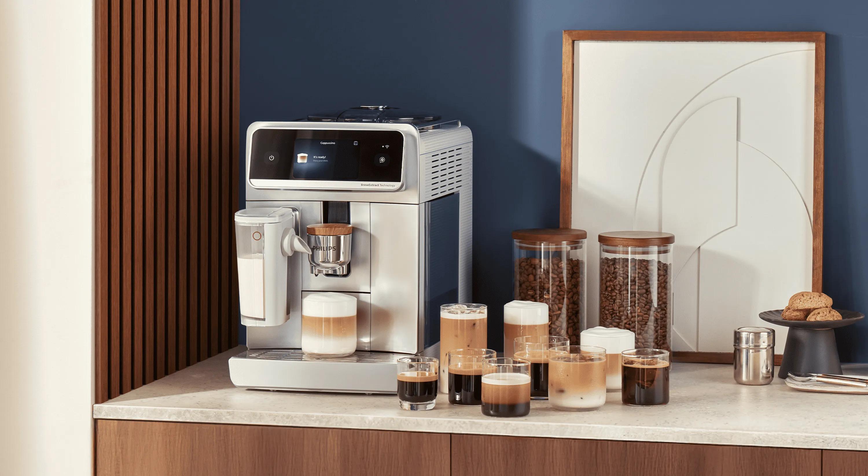 Ein Philips Kaffeevollautomat auf einer Küchenarbeitsplatte mit mehreren Tassen Kaffeegetränken, Gläsern mit Bohnen und einem Krug daneben.