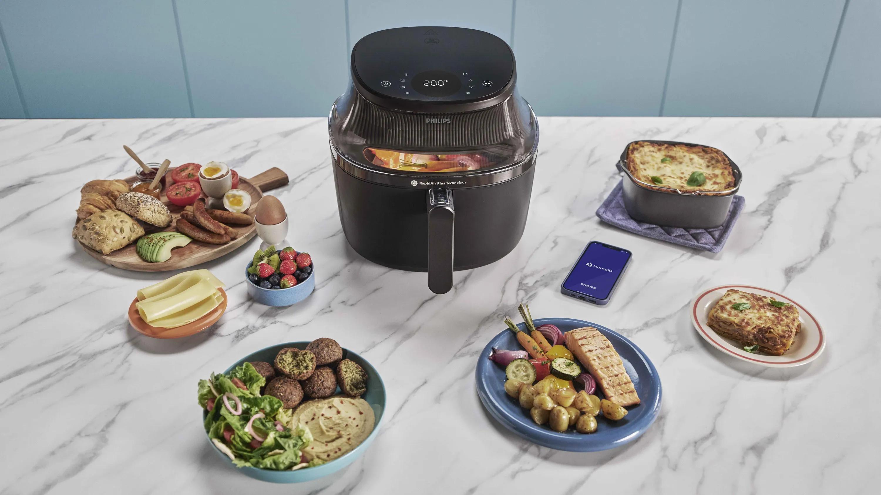 Philips Airfryer with various healthy dishes and HomeID app on marble kitchen counter.
