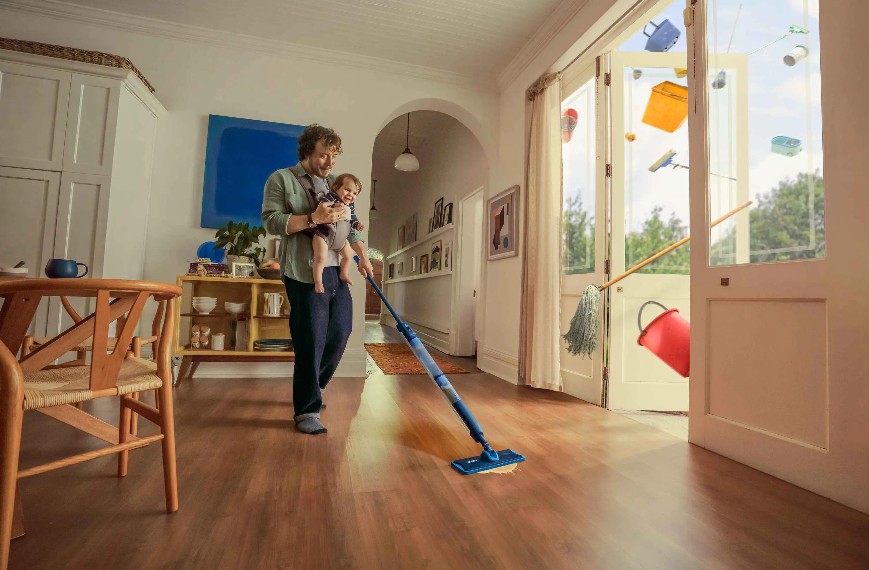 Philips OneUp Floor Care ad: Father holding baby while mopping floor, with cleaning supplies flying out of open doors.