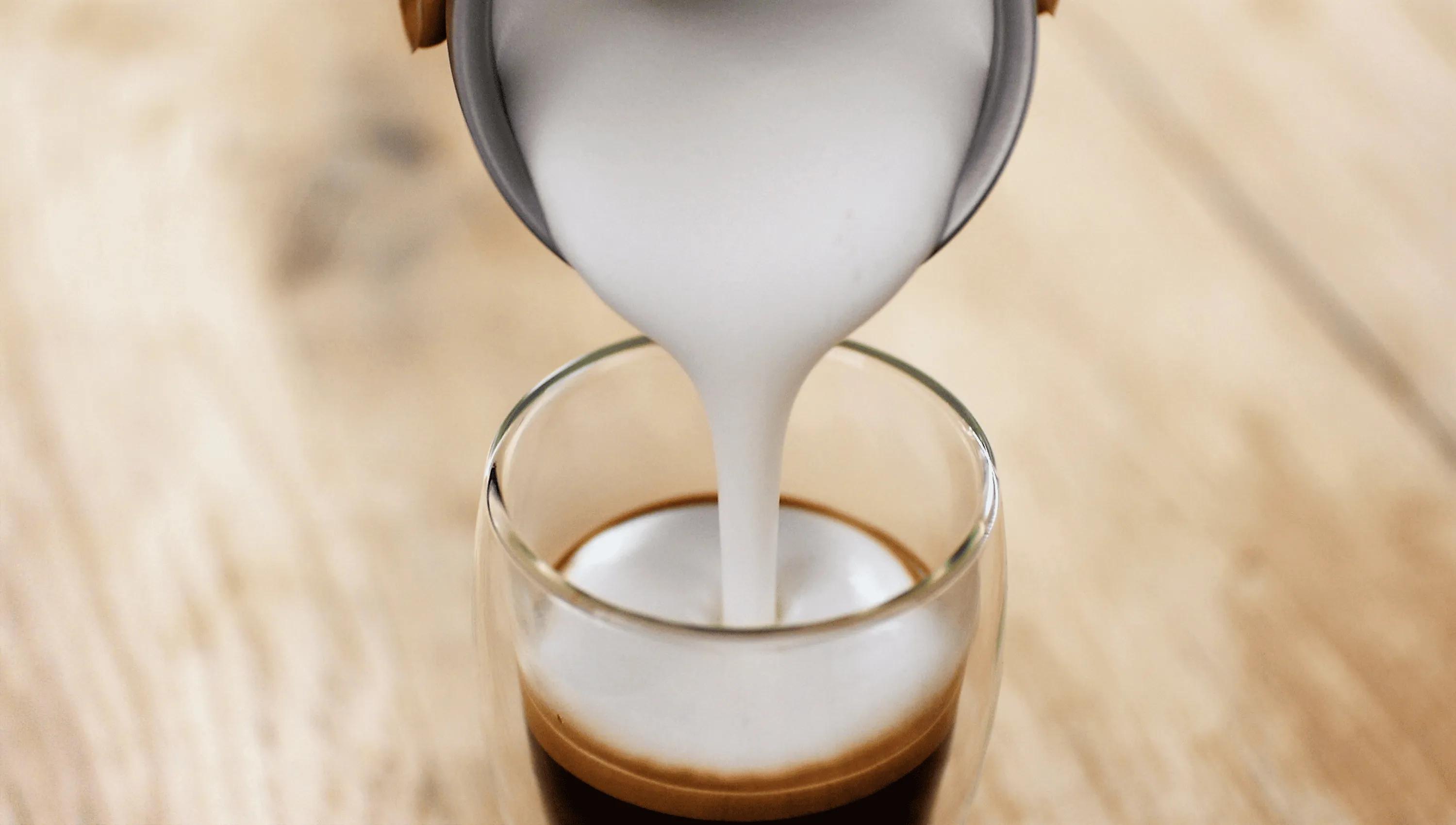 Close-up of creamy milk foam being poured into a freshly brewed espresso — perfect for creating a rich cappuccino or latte. Ideal for coffee lovers and premium espresso machines.
